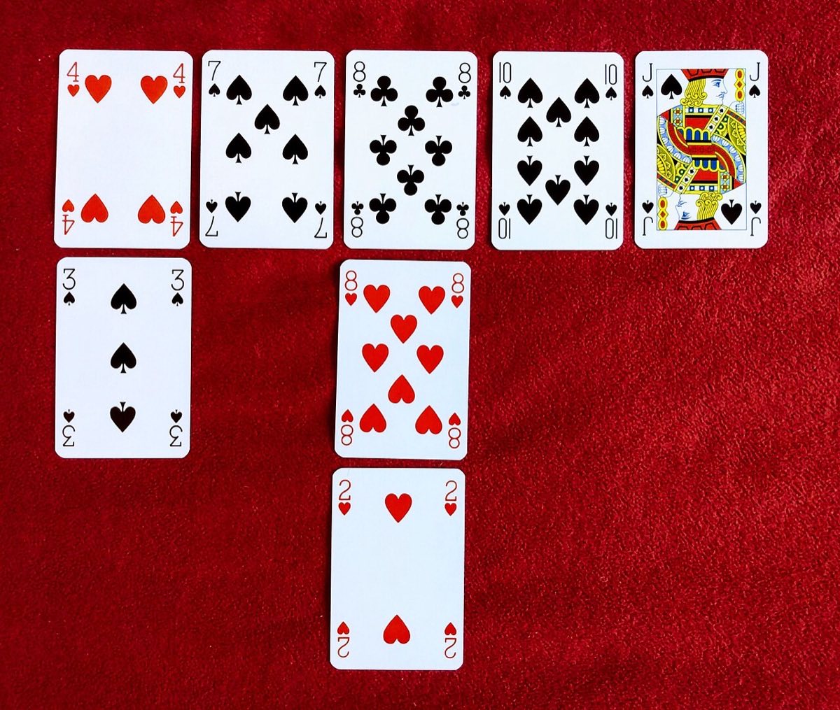 Photograph of an Eleusis game on a red cloth: a row of five accepted cards with rejected cards beneath the first and third