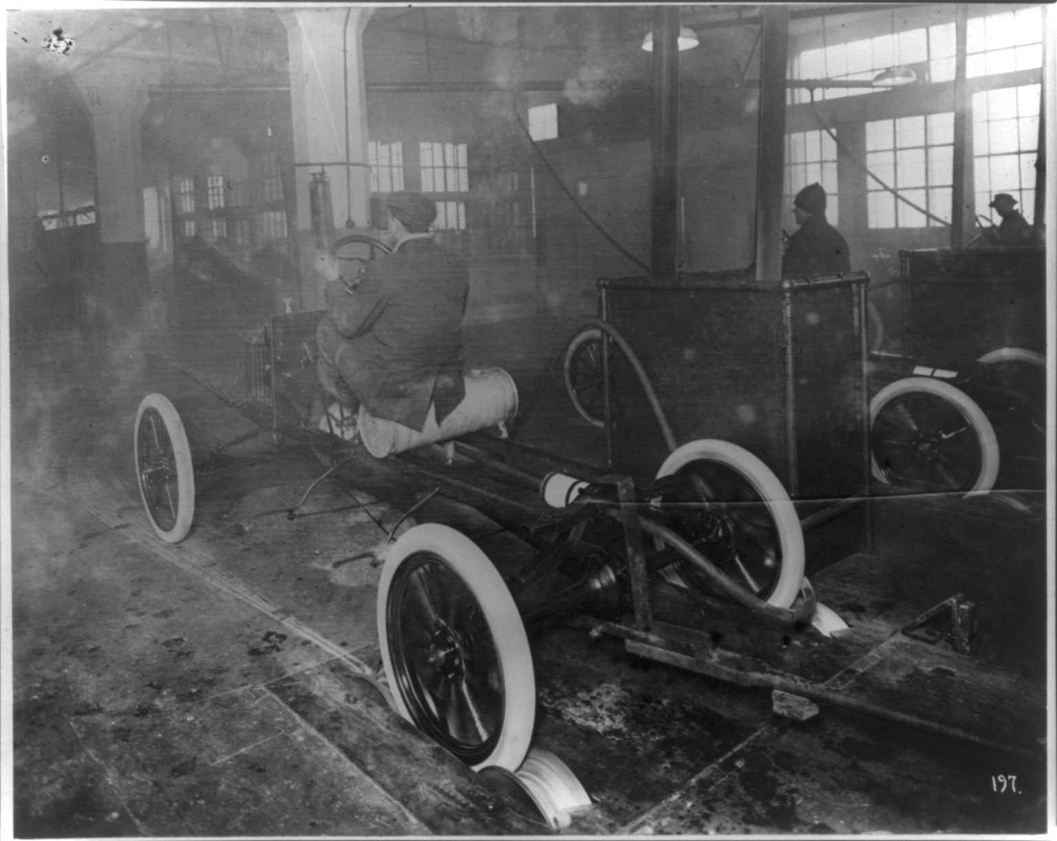 Men riding the bare chassis of a Model T as it comes off the assembly line at Ford's Highland Park plant