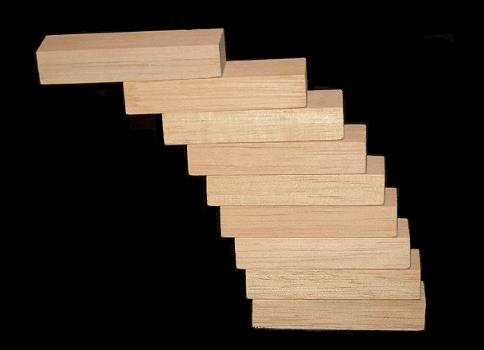 Photograph of identical wooden blocks stacked so that each sits farther out than the one below, the pile stepping sideways as it rises